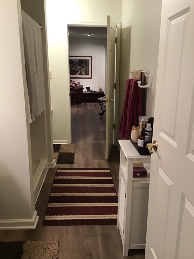 A hallway leading to a bathroom with a striped rug on the floor.