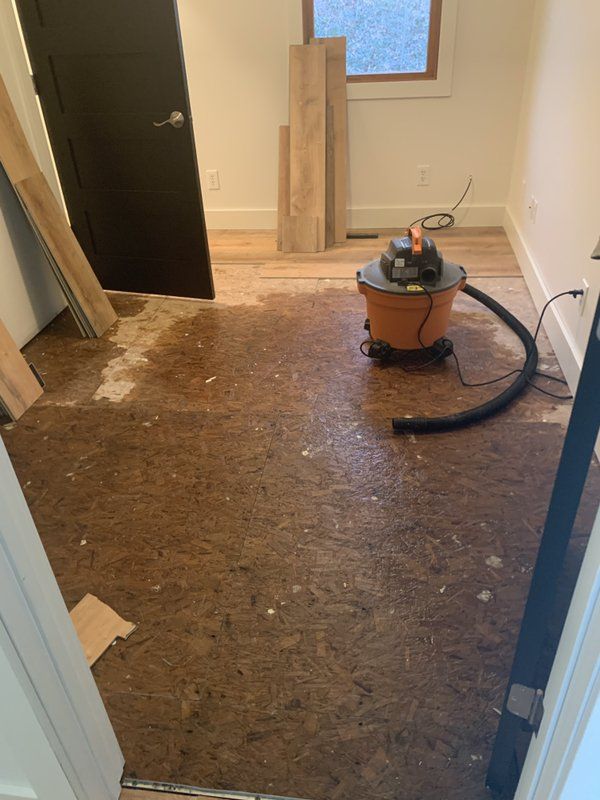 An industrial vacuum cleaner is sitting on a wooden floor inside a room.