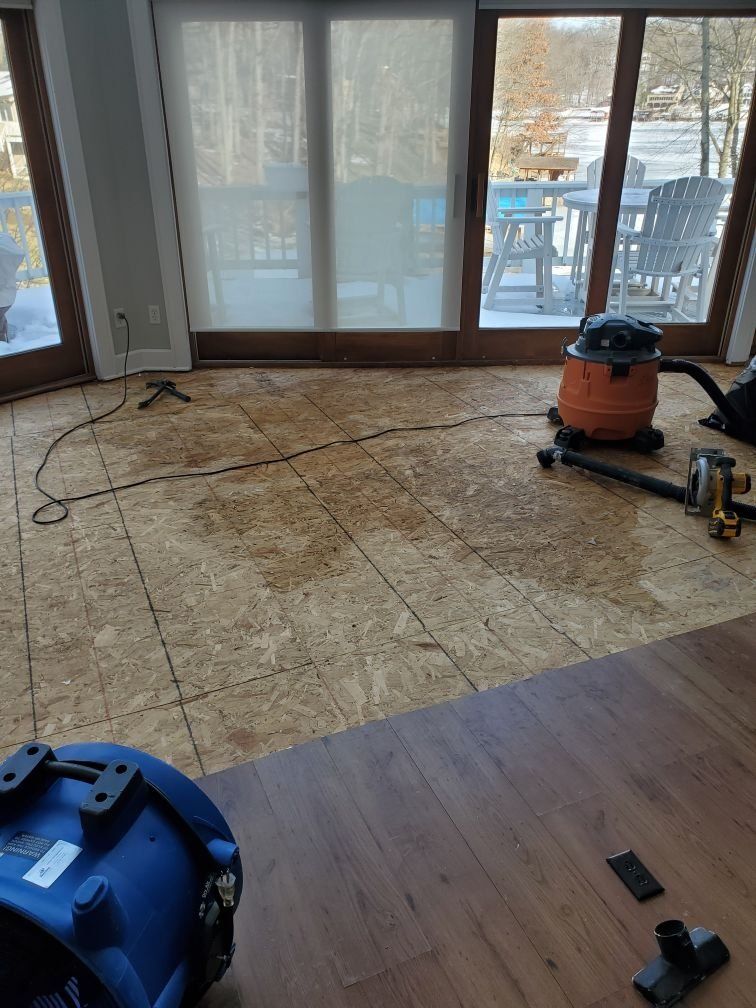 A living room with an industrial vacuum cleaner is sitting on a water damaged wooden floor.