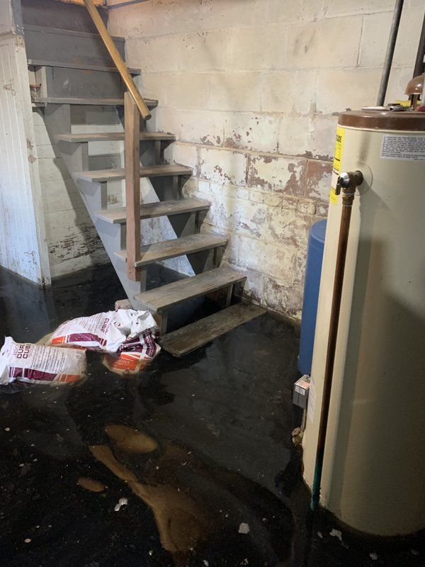 A flooded basement with stairs and a water heater.