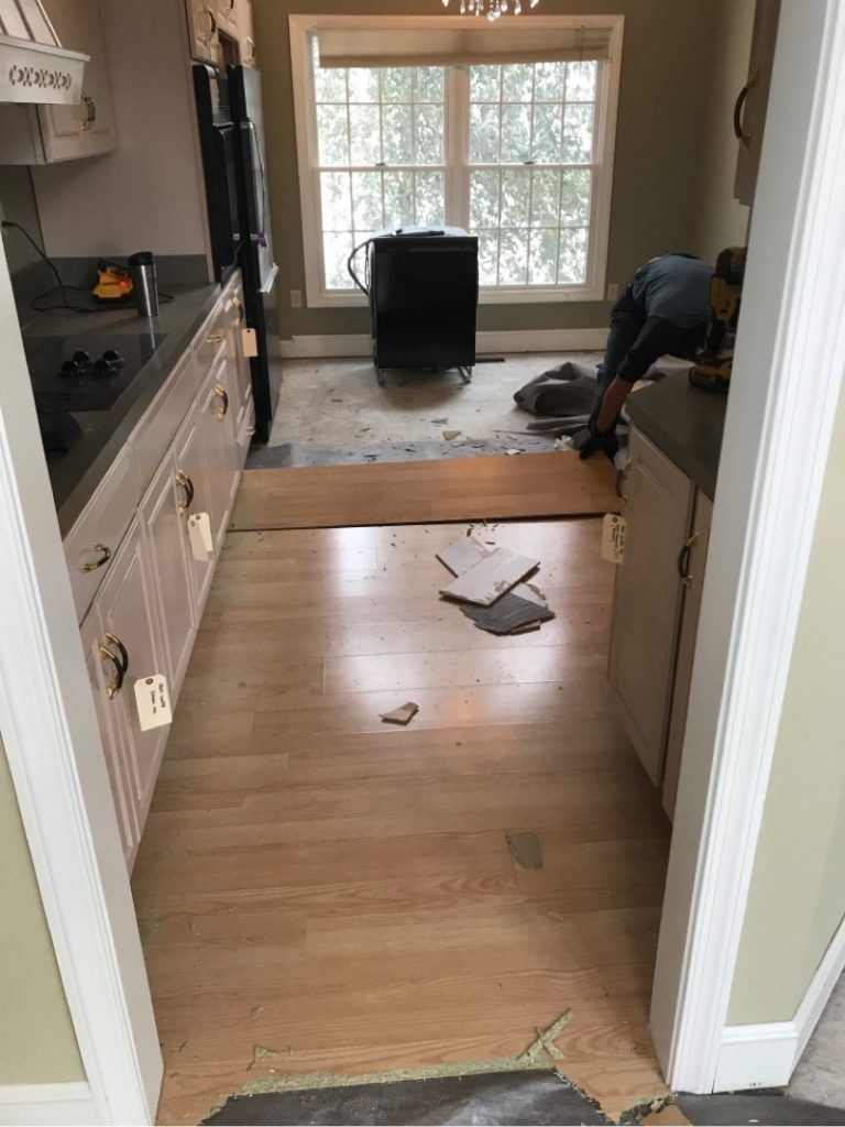 A man is working on a wooden floor in a kitchen.