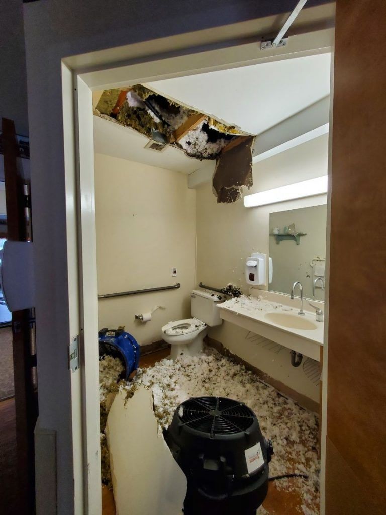 A water damaged bathroom with a toilet , sink , and ceiling damage.