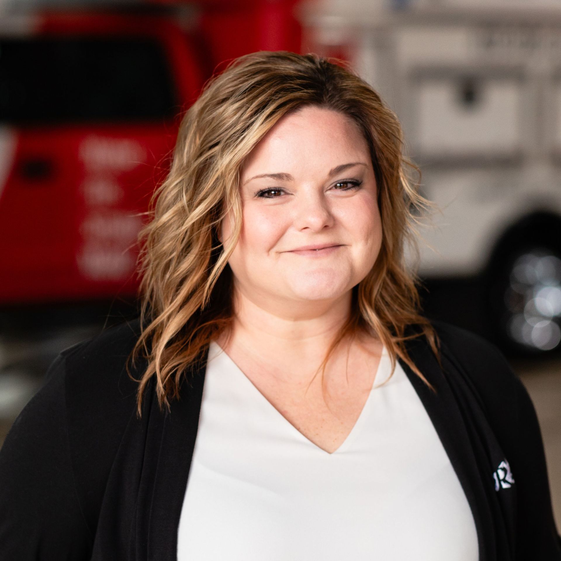 A woman in a white shirt and black jacket is smiling in front of a red truck.