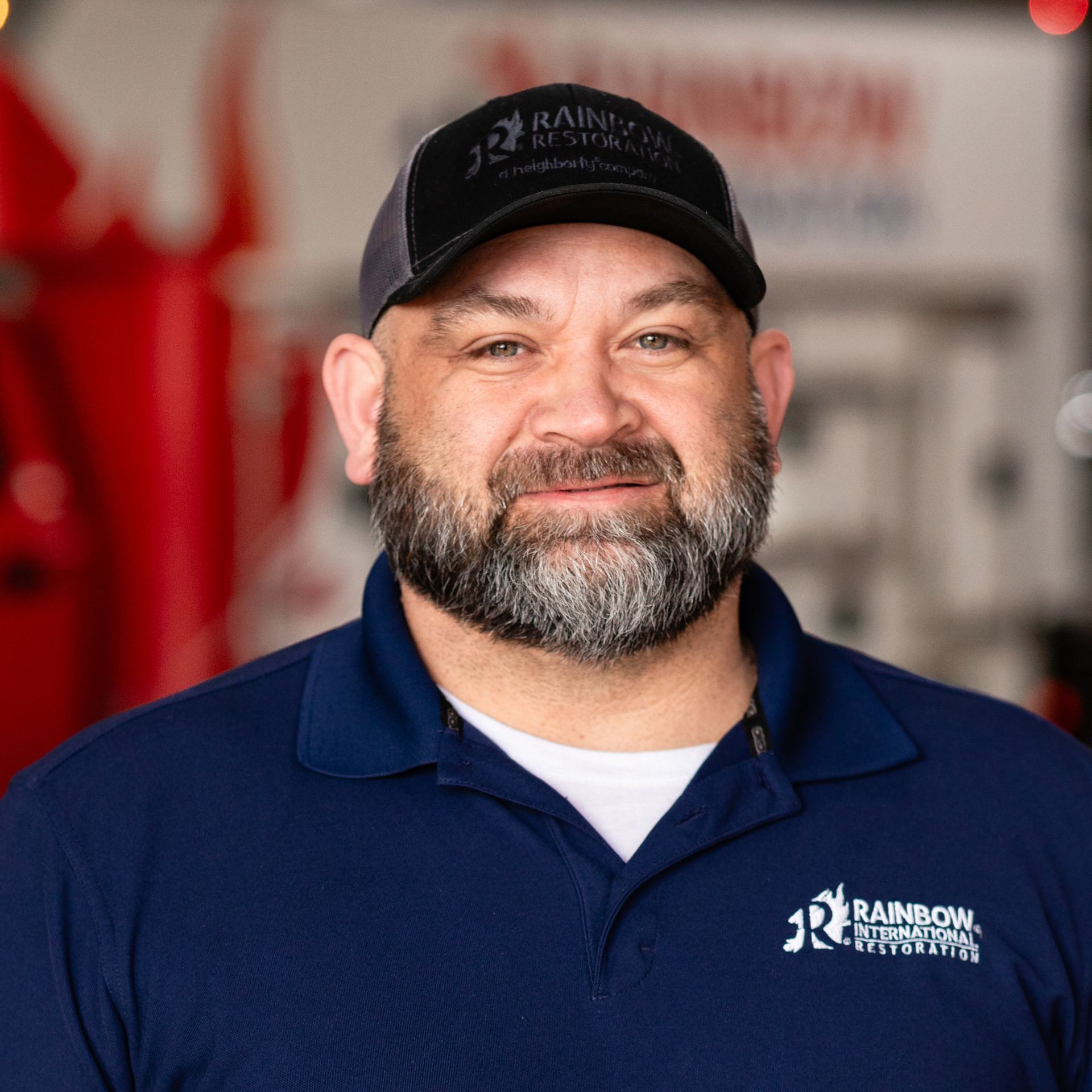 A man with a beard is wearing a hat and a blue shirt.