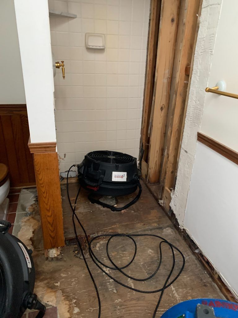 An industrial fan is sitting on the floor of a bathroom next to a toilet.