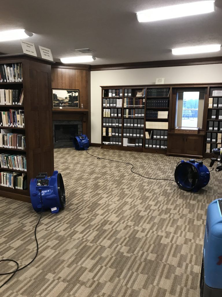 A library with bookshelves and blue industrial vacuums on the floor.