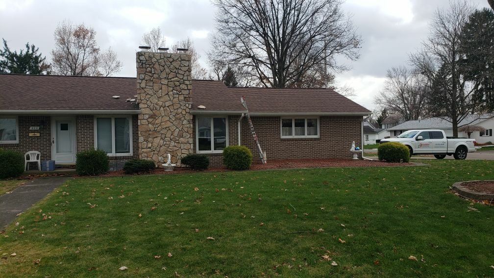 A white truck is parked beside a brick house with a chimney.
