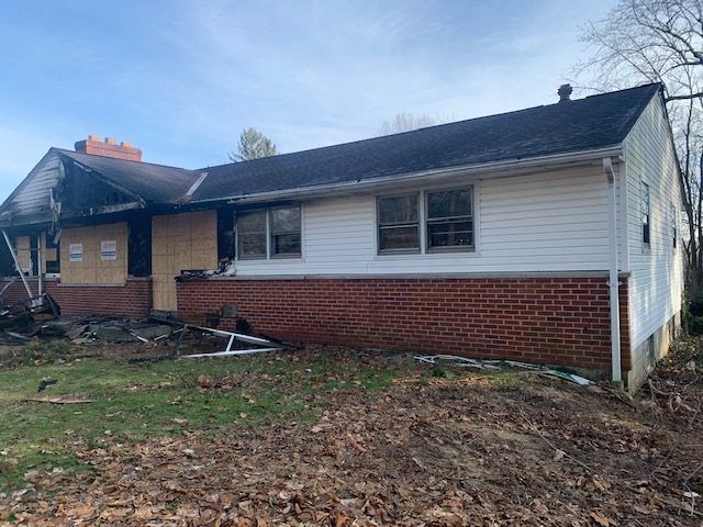 A fire damaged white house with a brick wall and a black roof.