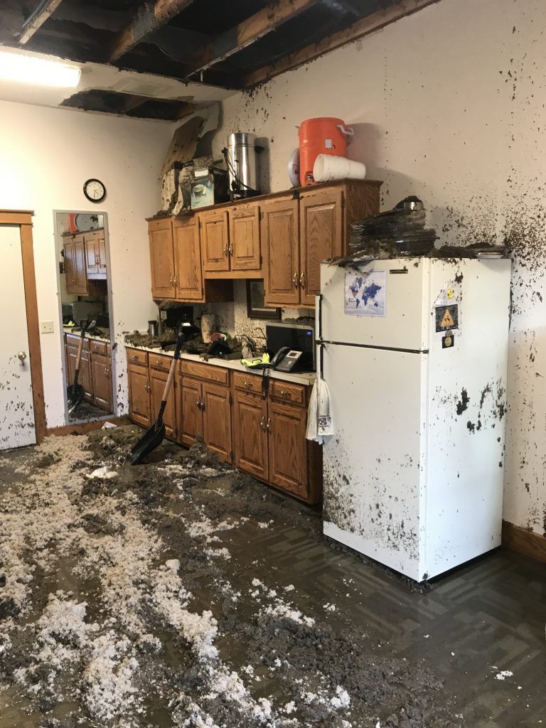 A water damaged kitchen with a white refrigerator and wooden cabinets.