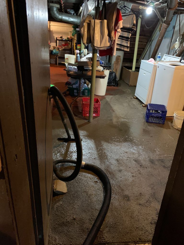 A dirty basement with a vacuum hose coming out of the door.