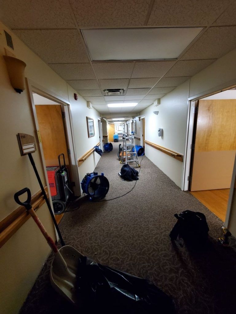 A long hallway with blue industrial drying fans and a ladder.
