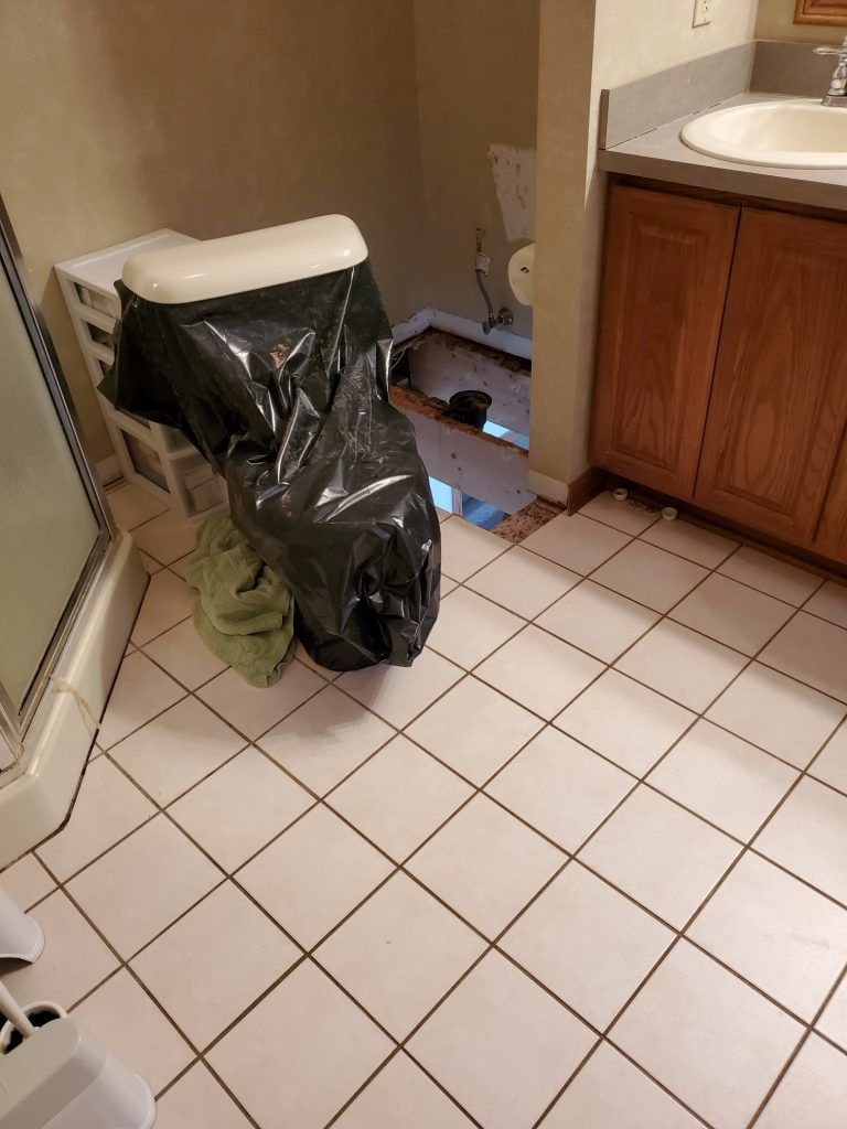 A bathroom with a toilet and a trash bag on the floor.