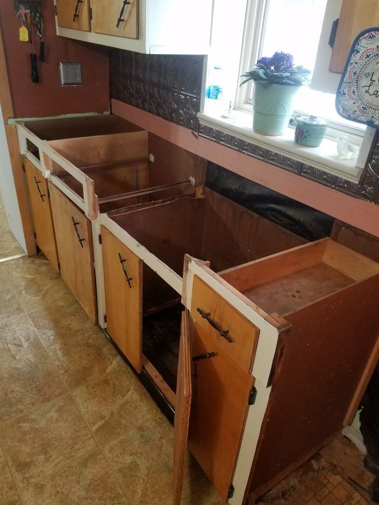 A kitchen being remodeled with a sink , cabinets , drawers and a window.
