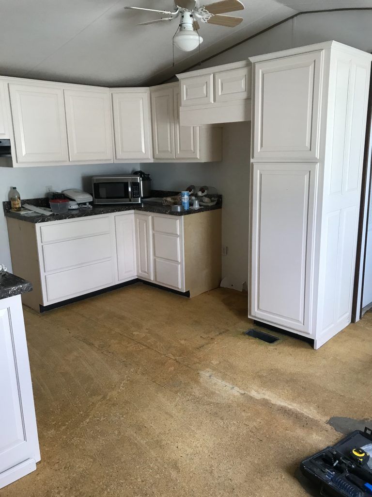A kitchen with white cabinets, a ceiling fan and stainless steel microwave.