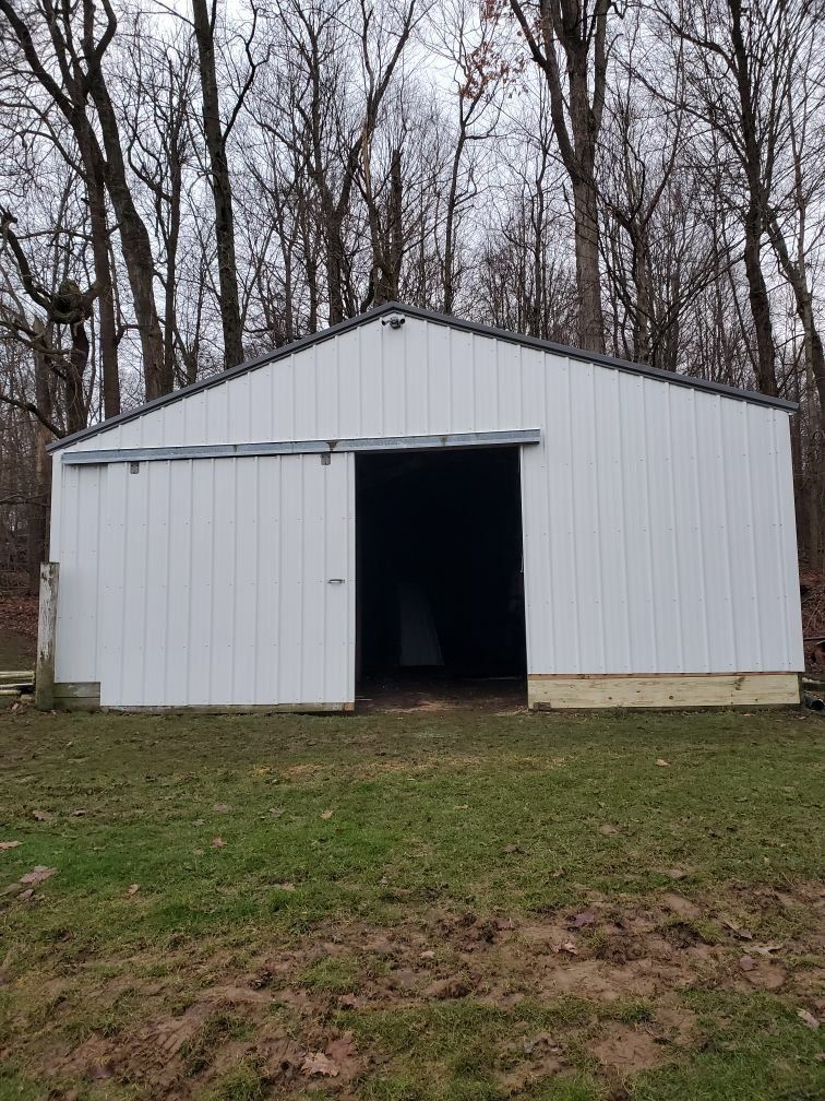 A white barn with a sliding door is sitting in the middle of a grassy field.