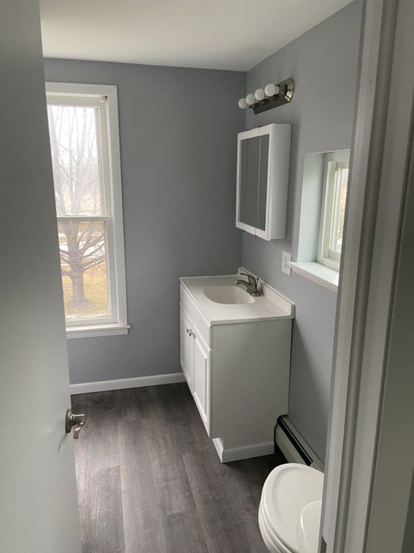 A bathroom with a sink , toilet , mirror and window.