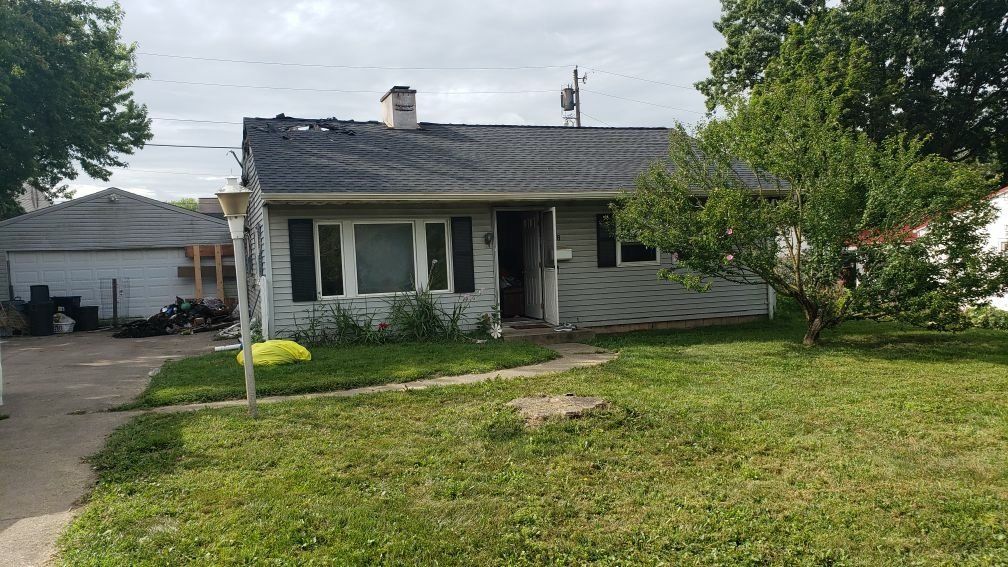 A white house with a gray roof and a large lawn in front of it.