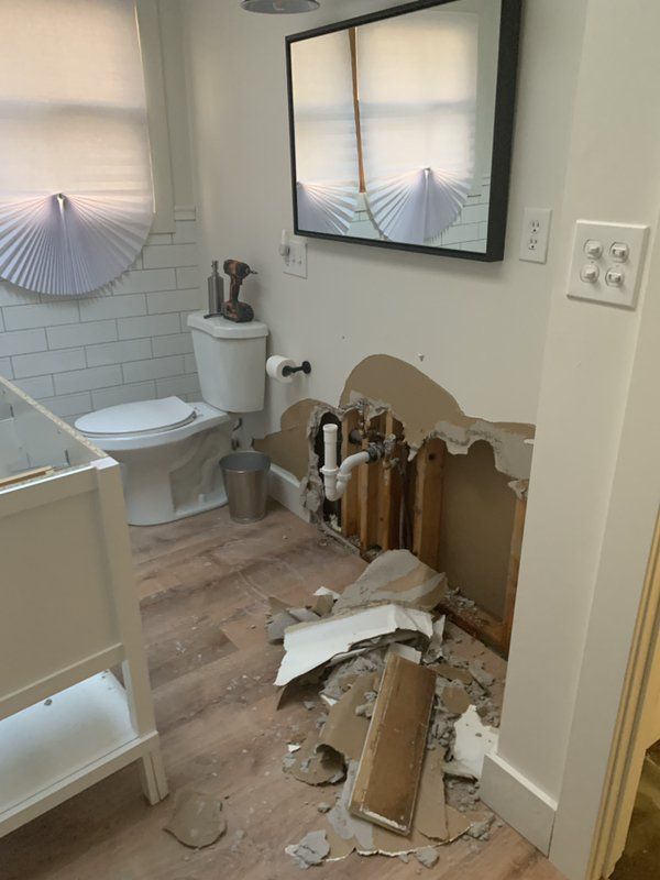 A bathroom with a toilet , sink , mirror and a broken wall.