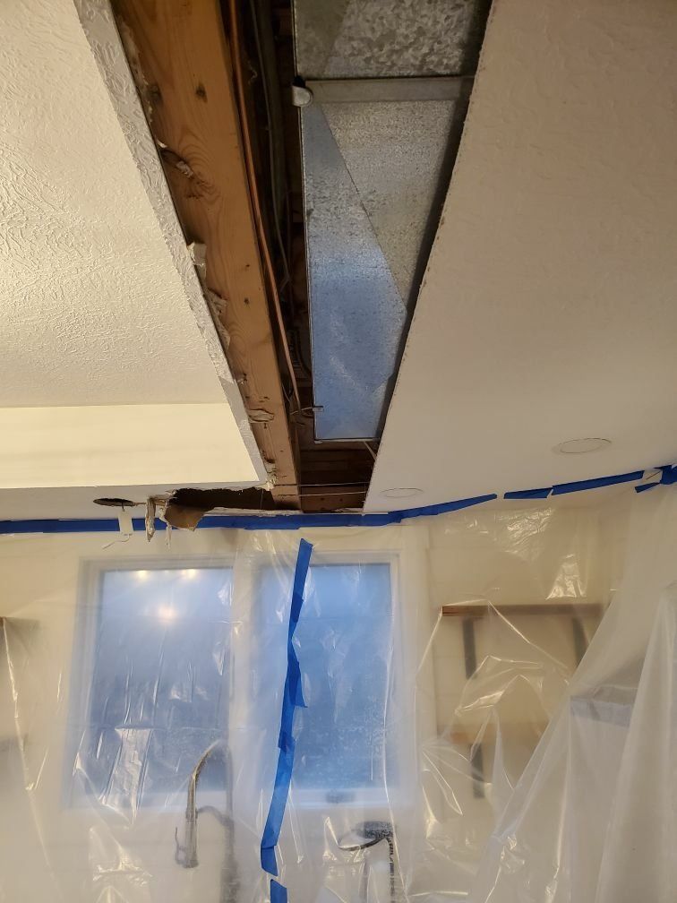 A kitchen with a hole in the ceiling and a window covered in plastic.