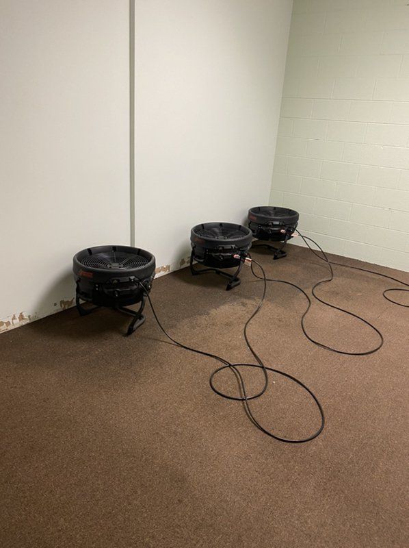 Industrial black fans sitting on the floor of water damaged room.