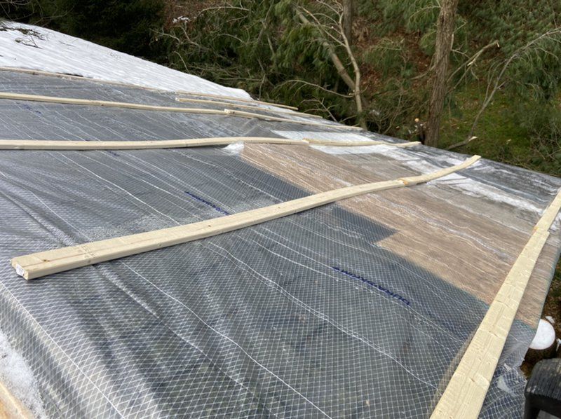 A barn roof that is being repaired from tree damage covered with plastic and wooden beams.