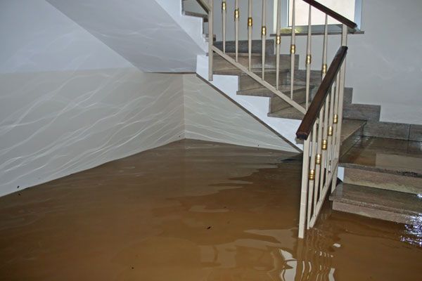 A flooded hallway with stairs and a railing covered in water.