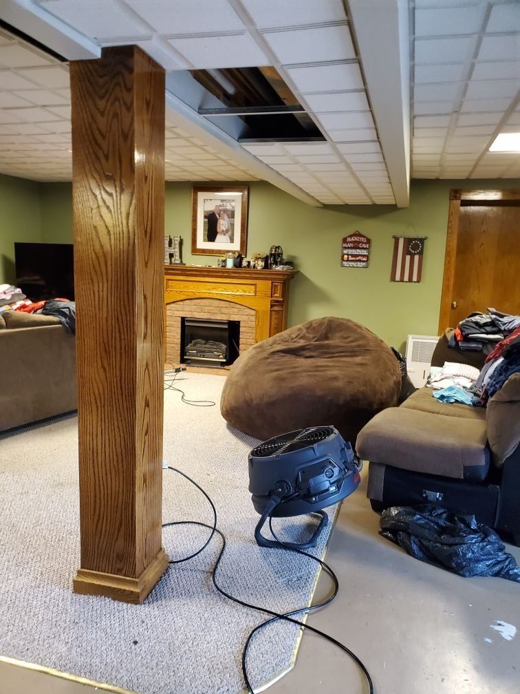 A living room with a wooden pillar in the middle of it, fireplace, tv, and industrial fan in it.
