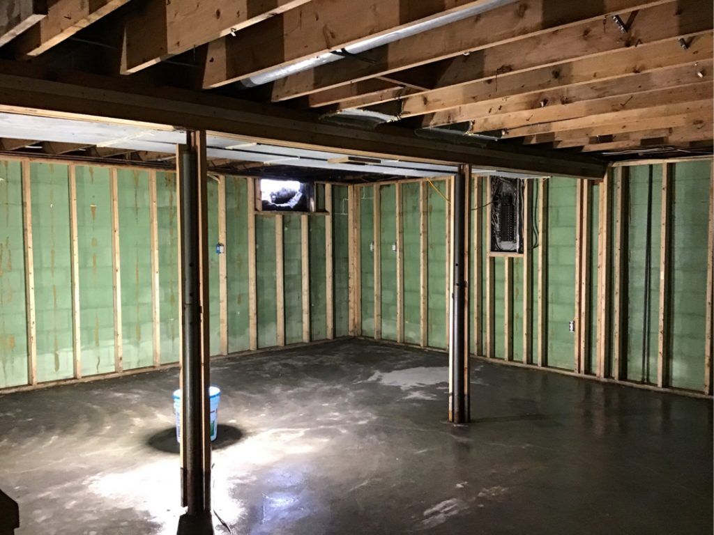 A basement under construction with green insulation and wooden beams.