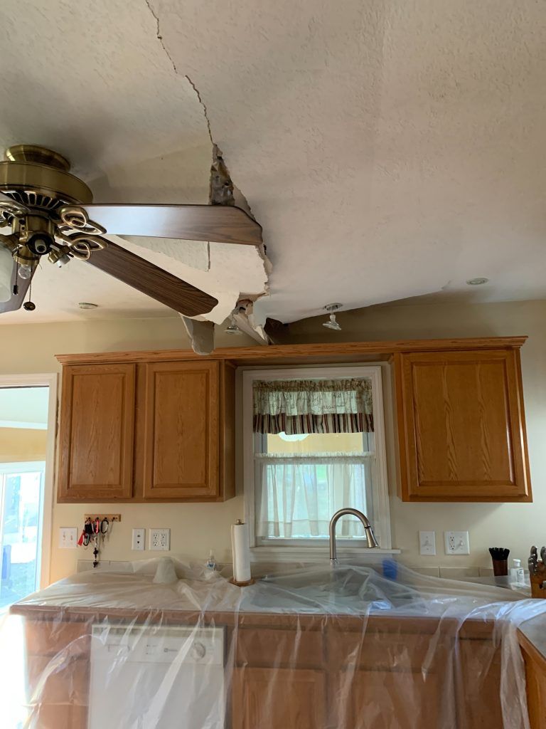 A kitchen with a damaged ceiling and a sink covered in plastic.