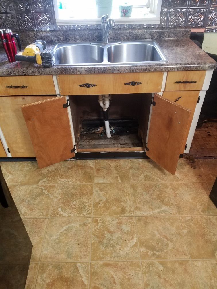 A kitchen sink is under a cabinet with the door open and water damage within.  