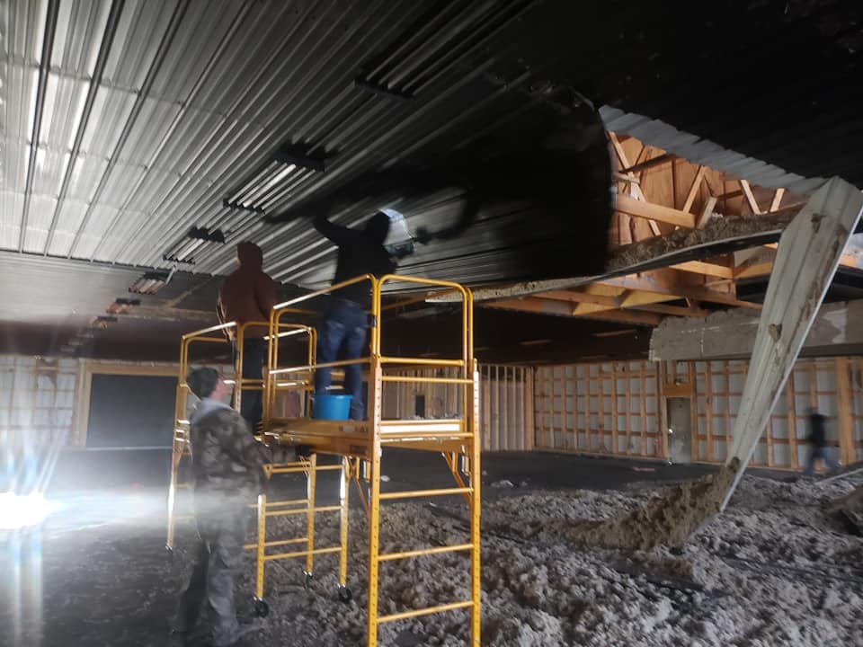 Two construction workers are working on the ceiling of a building.