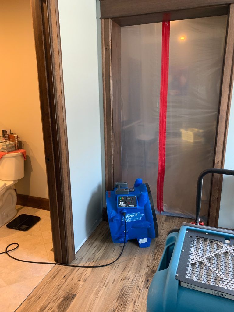 An industrial blue fan is sitting in a bathroom next to a toilet.