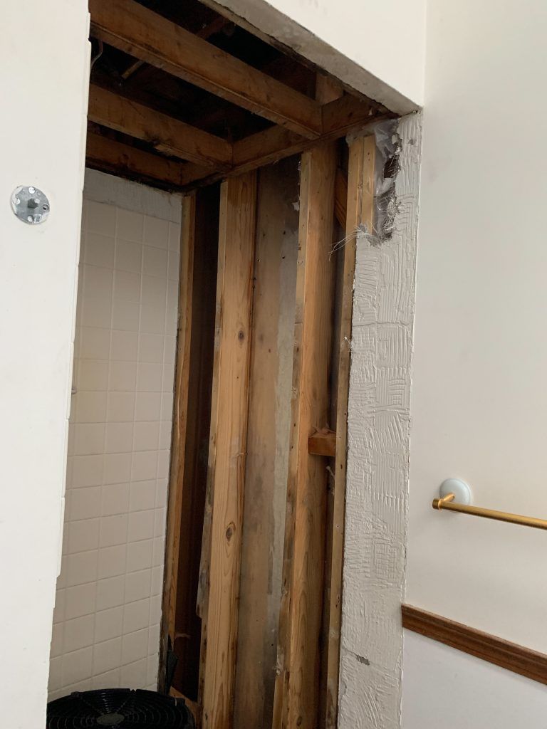 A bathroom with a towel rack and broken wall caused by water damaged.