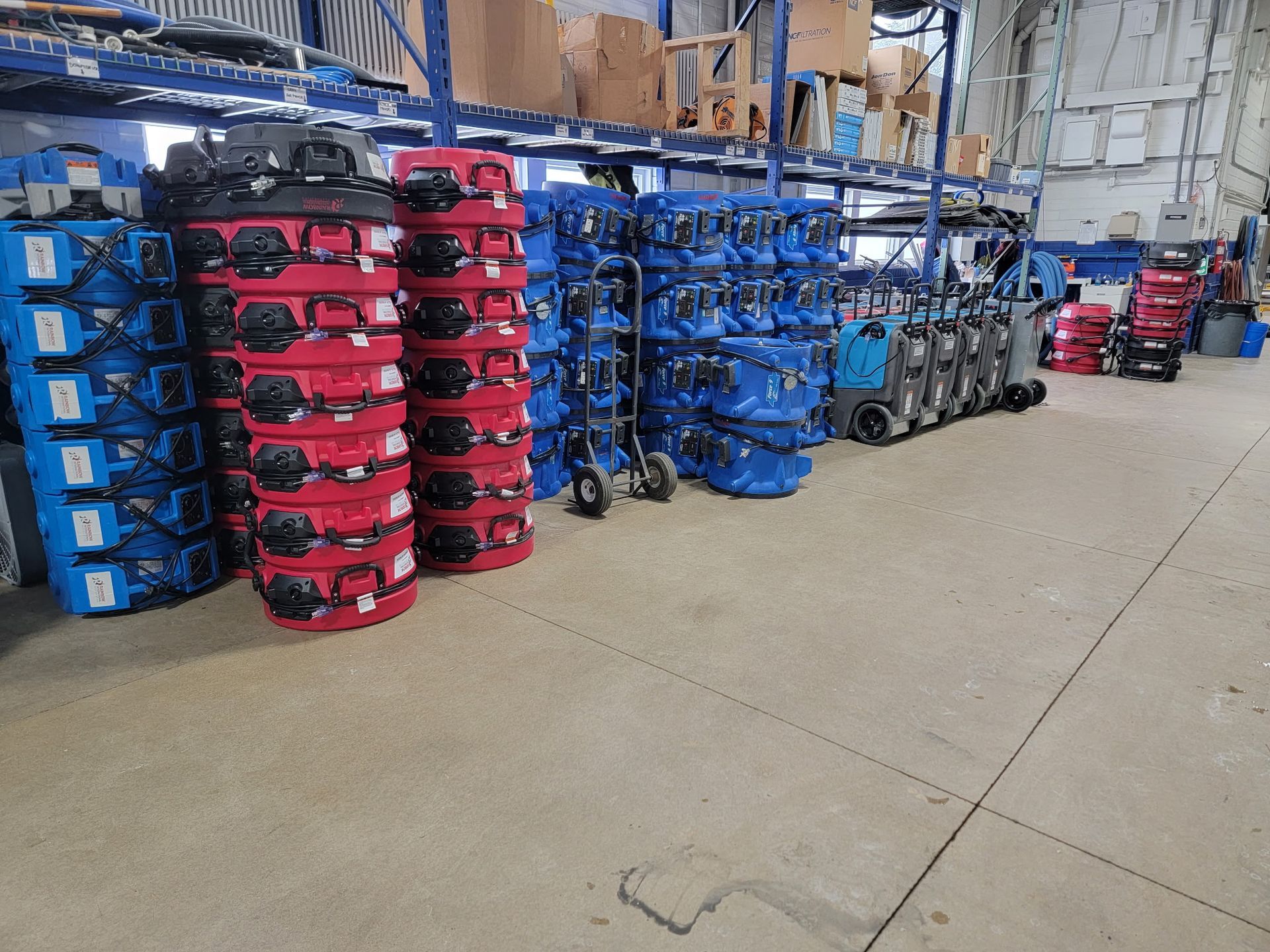 A row of blue industrial fans are sitting next to a wooden wall being repaired from water damage. 