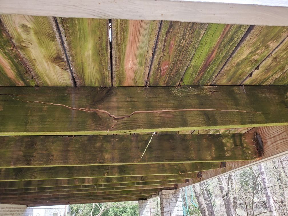 The bottom of a wooden deck with moss growing on it.