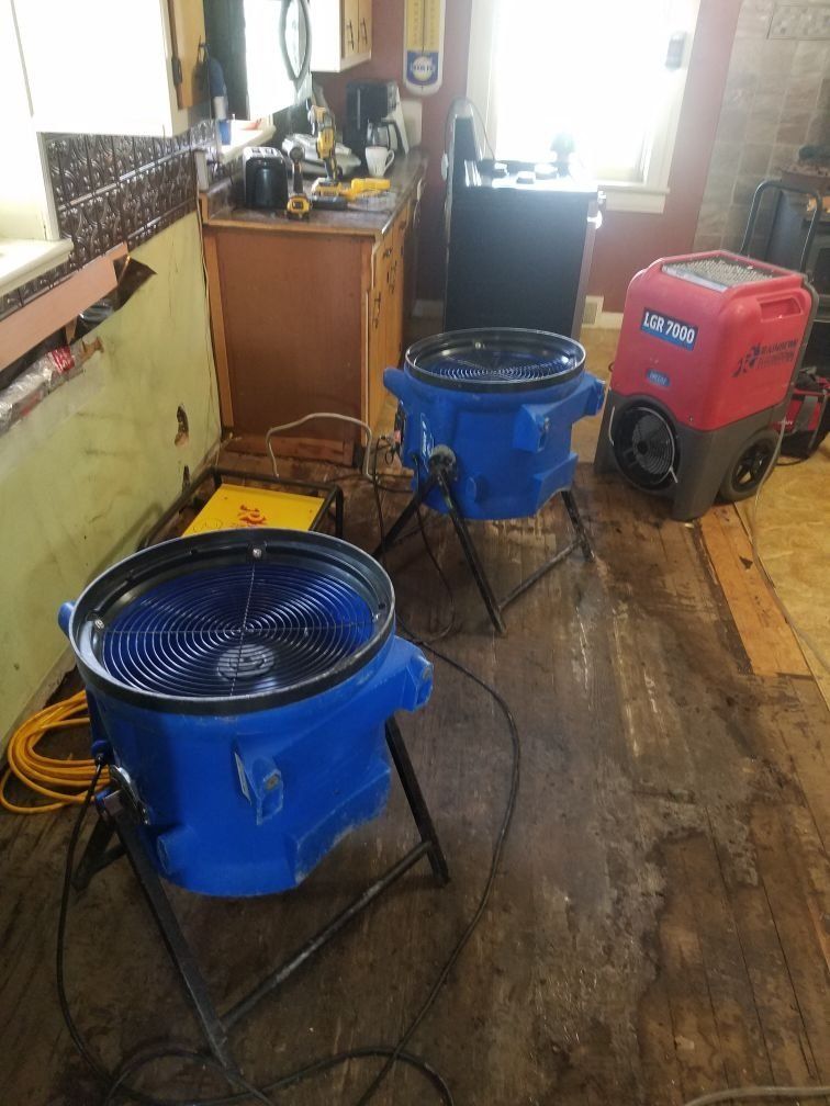 Two blue industrial fans are sitting on a wooden floor in a room.