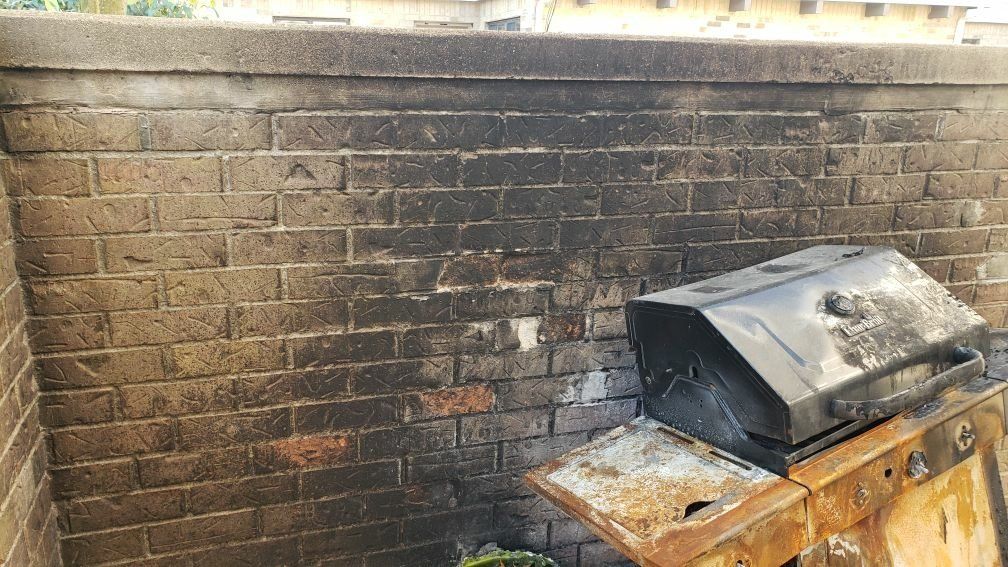 A fire damaged grill is sitting in front of a brick wall.