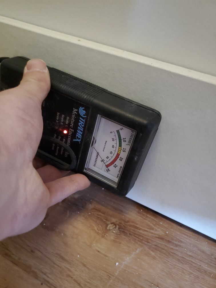 A person is holding a moisture meter on a wooden floor.