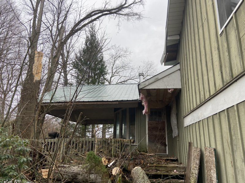 A house with a roof that has been damaged by a tree.