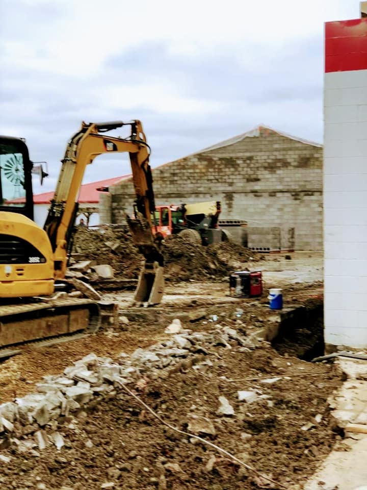 A yellow excavator is working on a construction site next to a building.