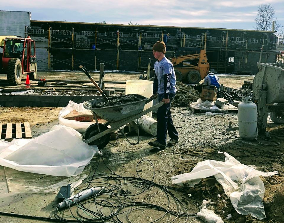 A man in a hat is pushing a wheelbarrow on a construction site.