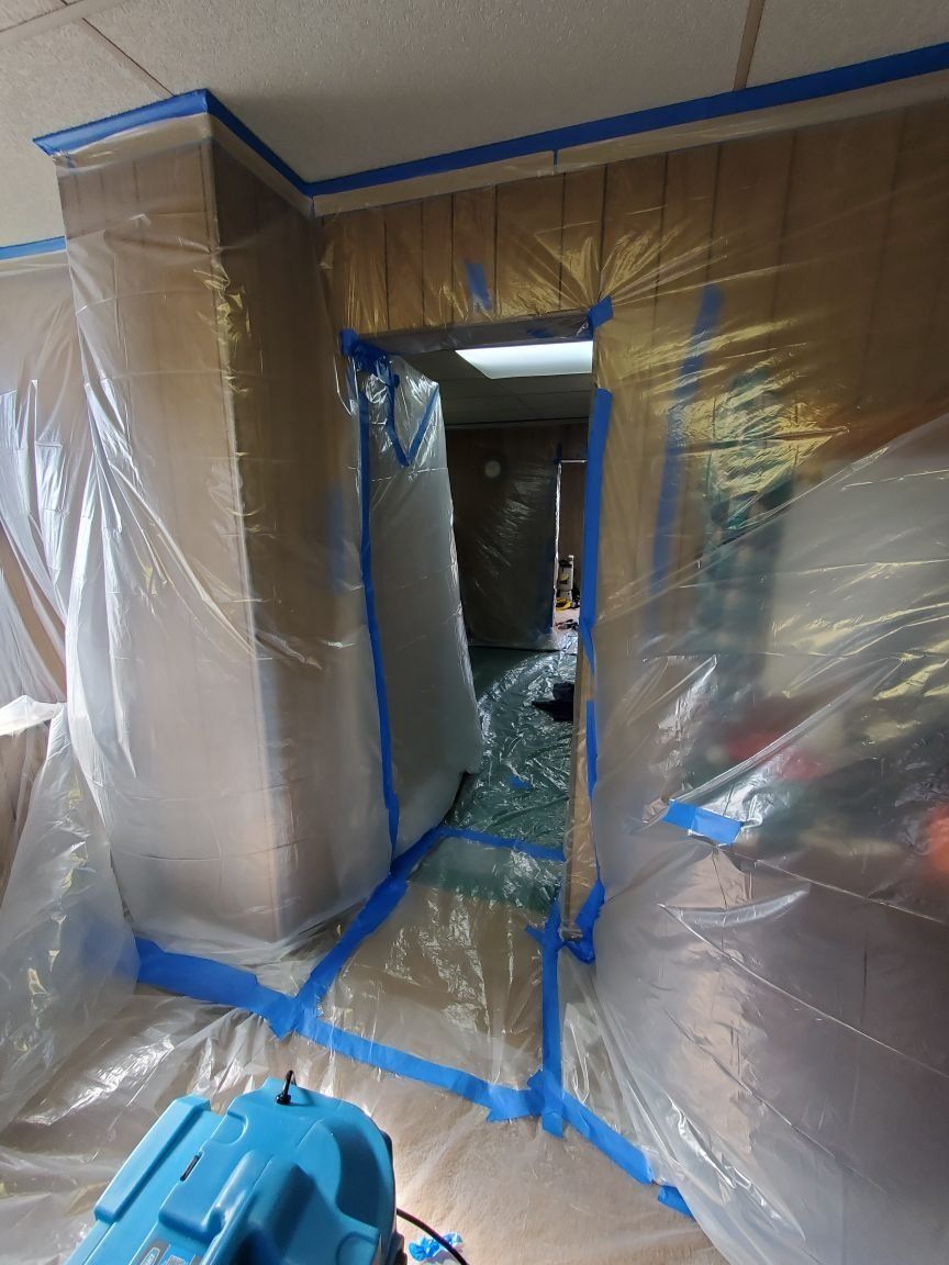 A room is covered in plastic and blue tape.