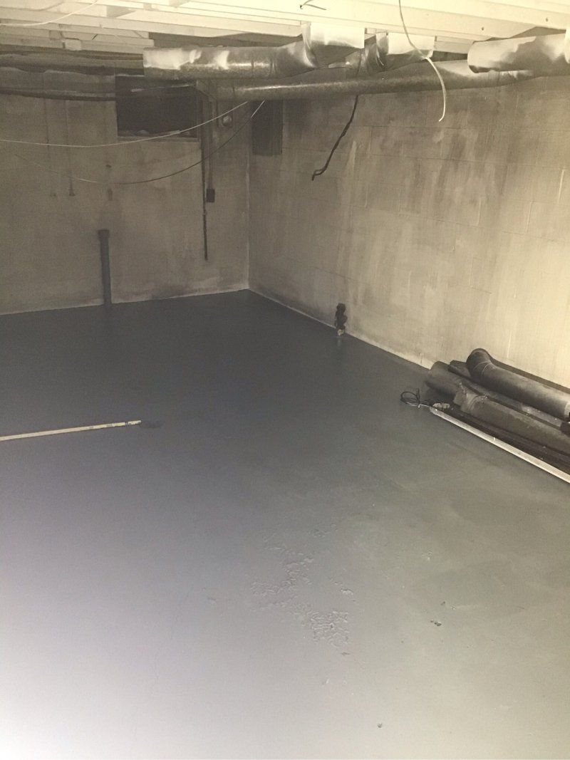 An empty basement with a gray floor and a concrete wall.