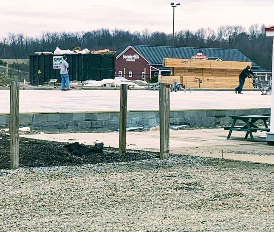 A picture of a person standing in front of a dumpster with large stacks of wood and a red boiling in the background.
