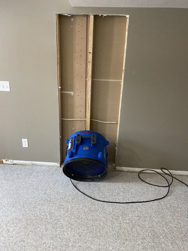 An industrial blue fan is sitting in a room next to a wall.