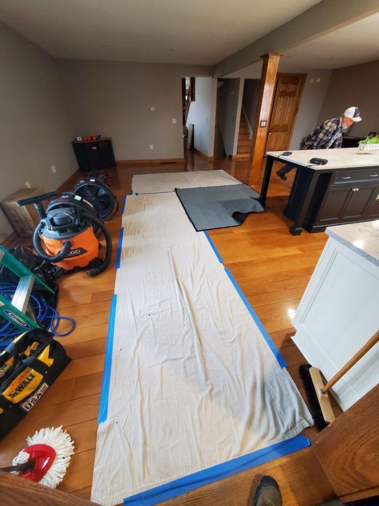 A living room with industrial vacuum, ladder and a mop on the floor.