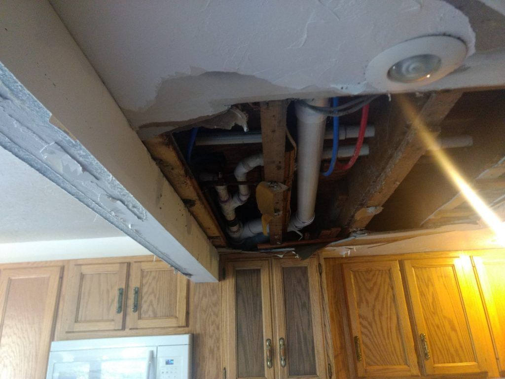 A kitchen with water damage containing wooden cabinets and a ceiling with pipes coming out of it.