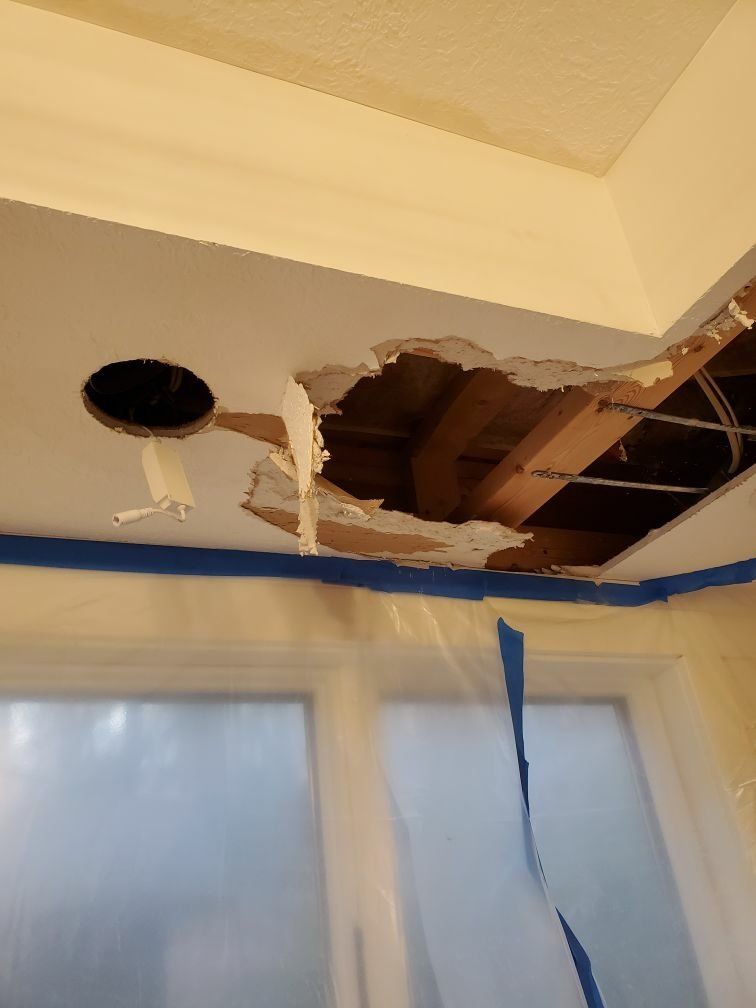 A damaged room with a hole in the ceiling and a window.