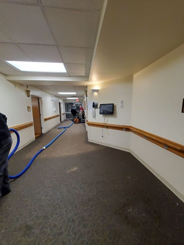 A man is using an industrial vacuum cleaner in a long hallway.