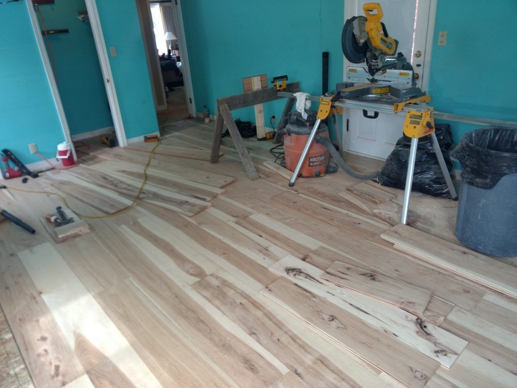 A room with a wooden floor, saw, and a saw horse on the floor.
